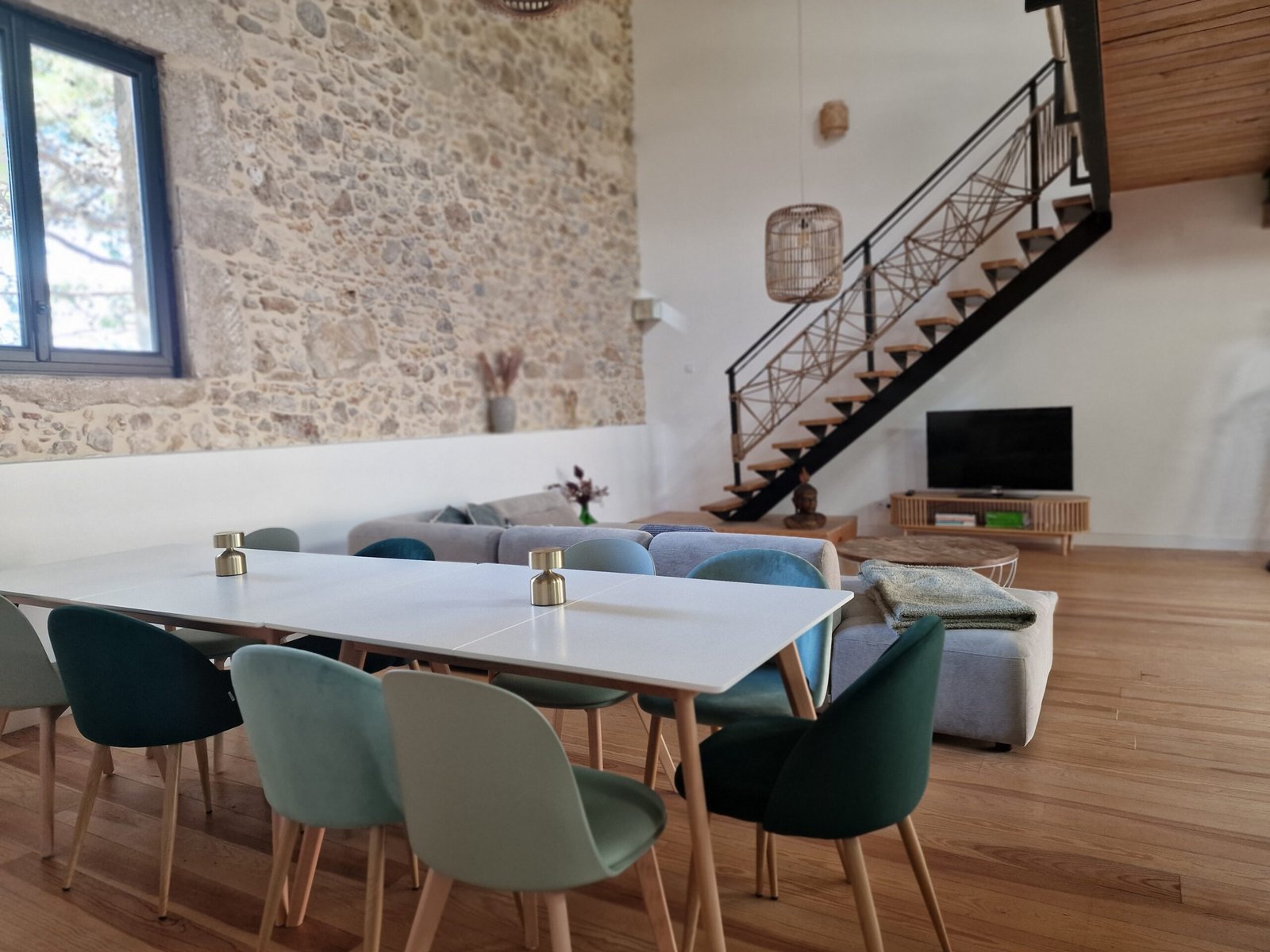 Grande table à manger dans la pièce de vie avec mur en pierre et salon d’un gîte de groupe à Narbonne