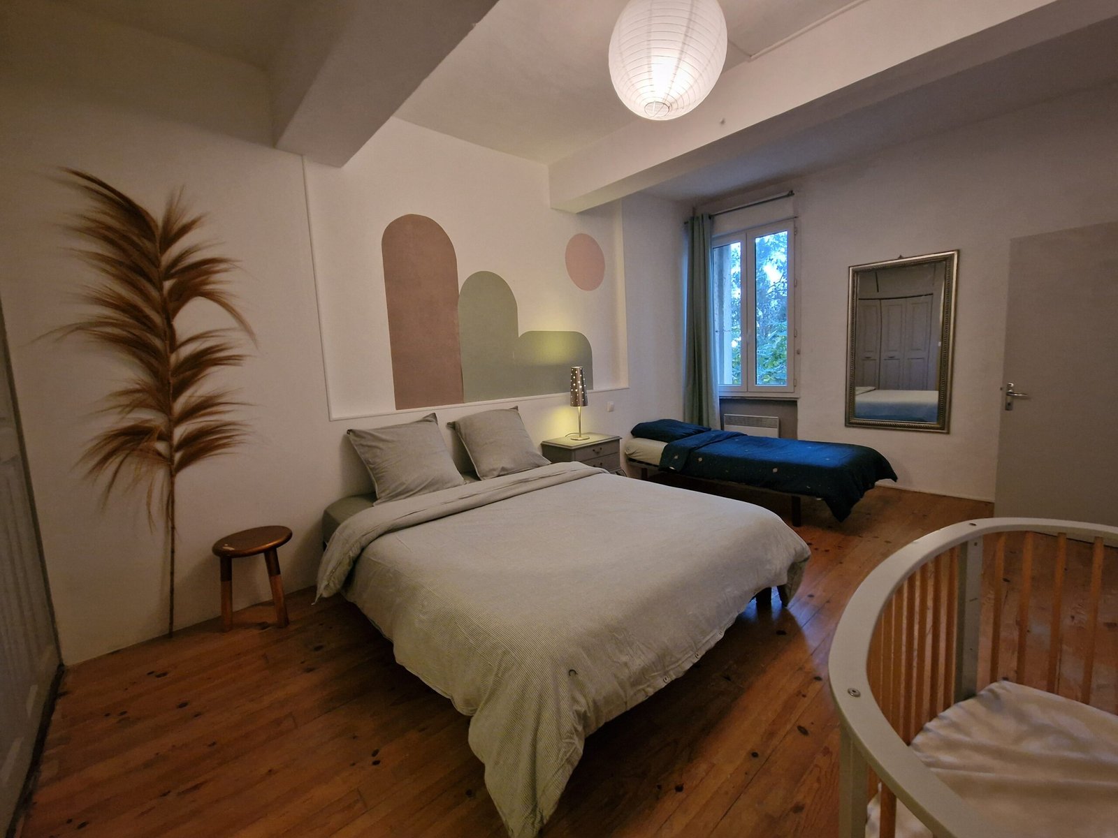 Chambre d’un gîte à Narbonne aménagée pour un séjour en famille, avec lit double, lit simple et lit bébé.