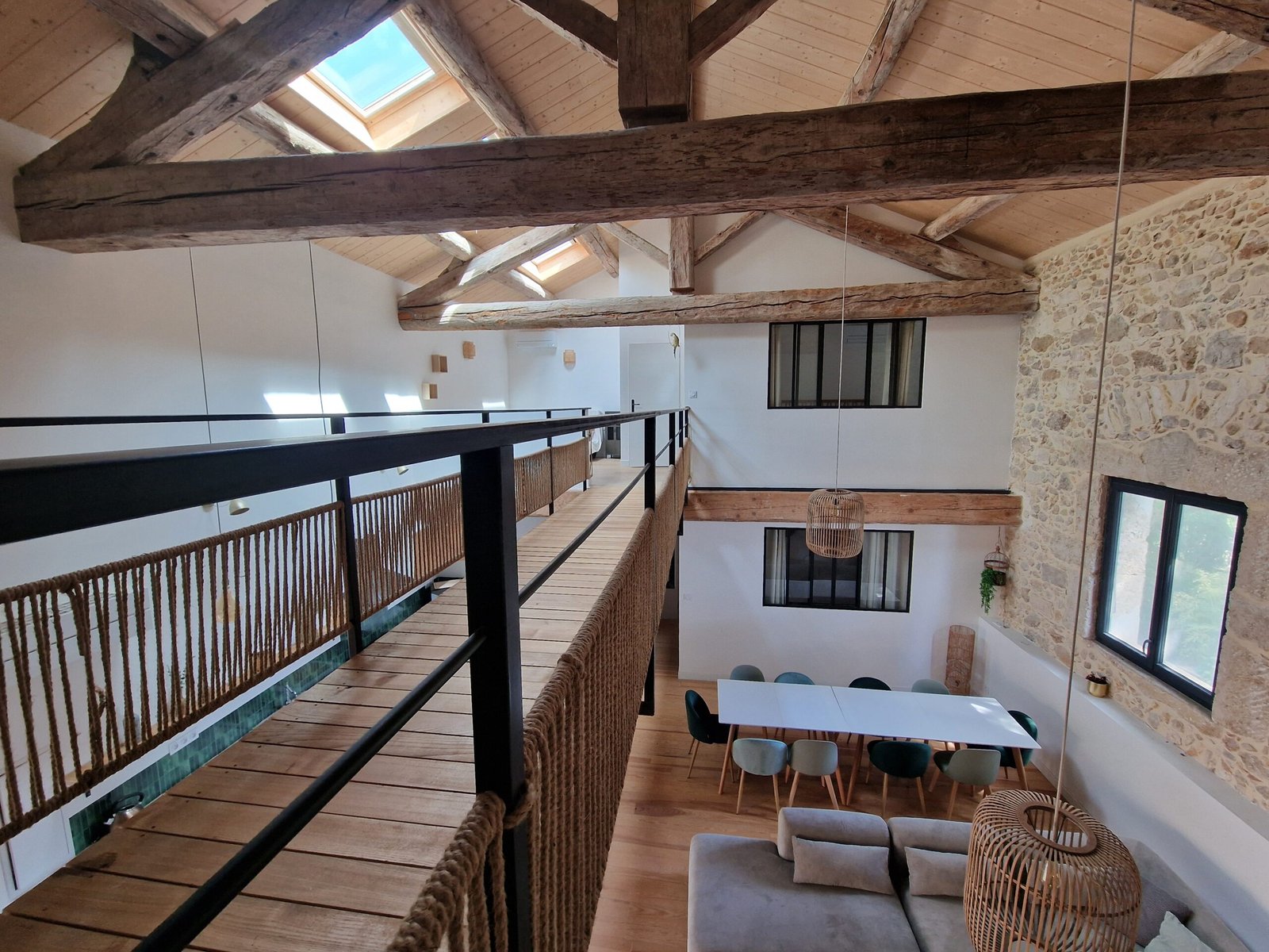 Passerelle en bois surplombant le séjour du gîte à Narbonne, sous une charpente ancienne avec mur en pierre apparente.