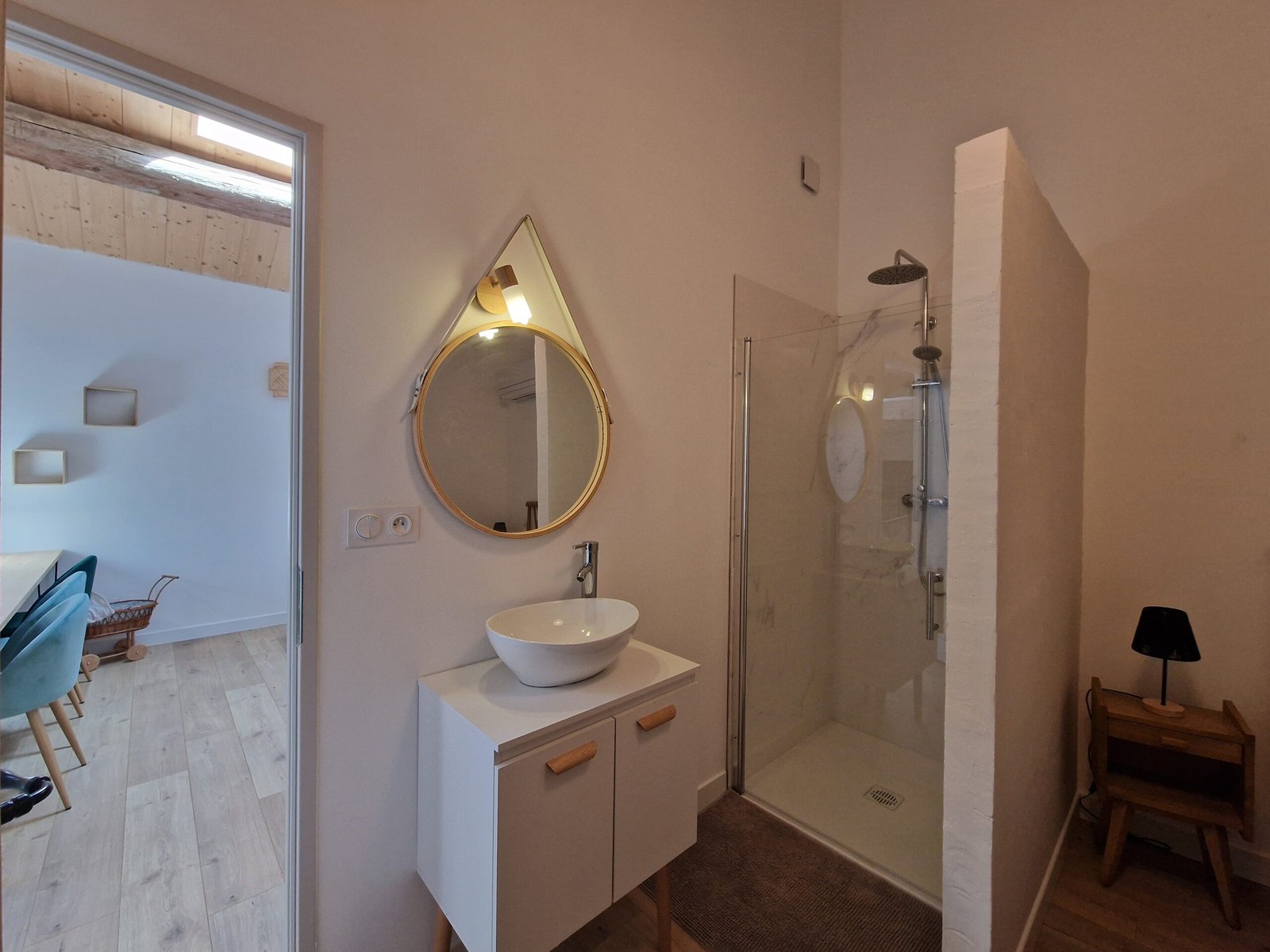 Salle de bain du gîte à Narbonne avec douche à l’italienne, vasque et grand miroir rond.
