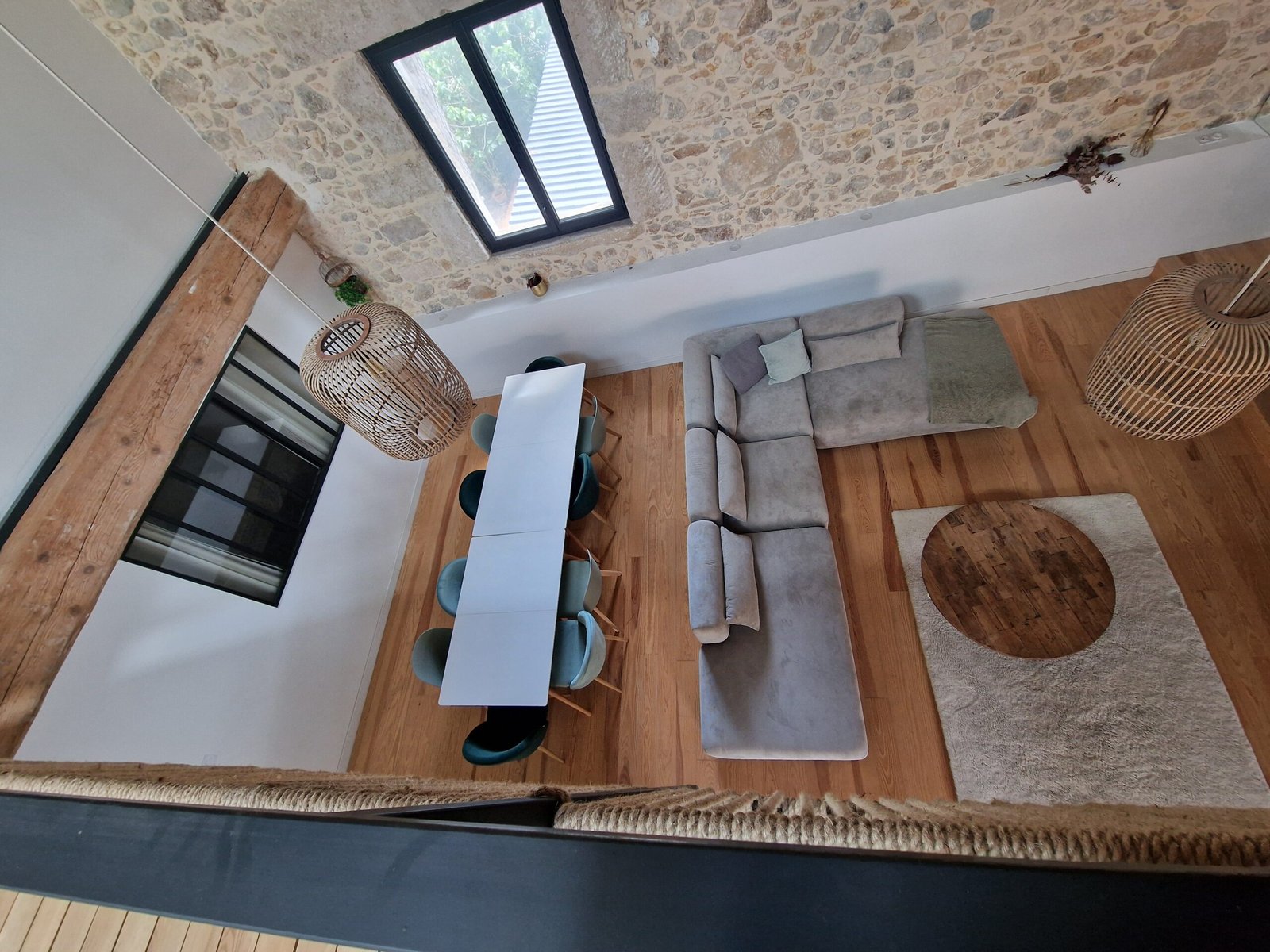 Vue depuis la passerelle sur le salon et la grande table du gîte à Narbonne, avec mur en pierre et parquet en bois.