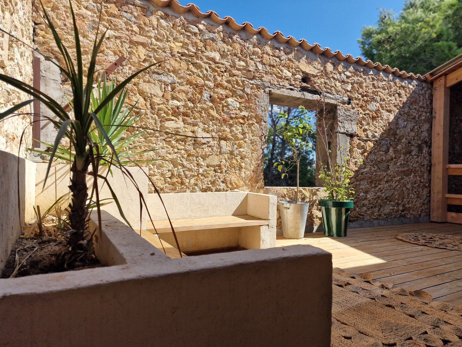 Coin détente extérieur du gîte à Narbonne avec banquette maçonnée, terrasse en bois et murs en pierre.