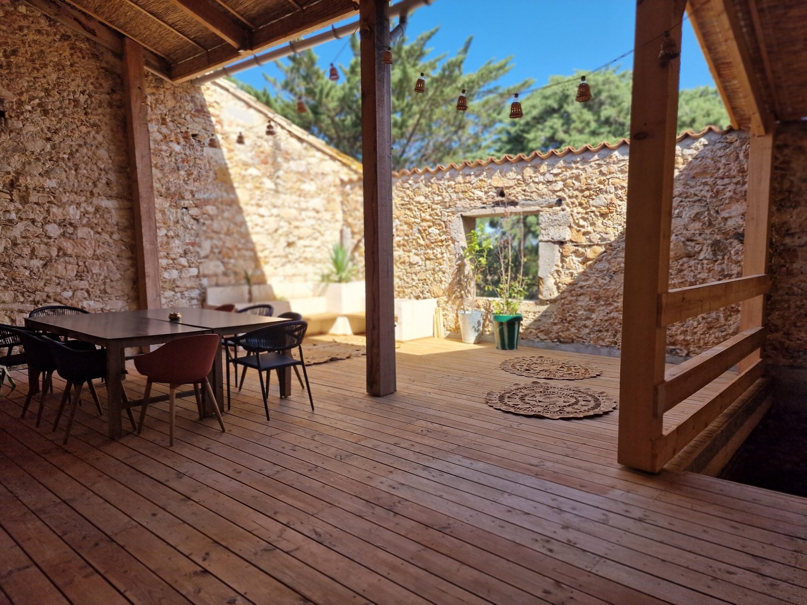 Terrasse couverte du gîte à Narbonne avec murs en pierre, terrasse en bois et espace repas extérieur.